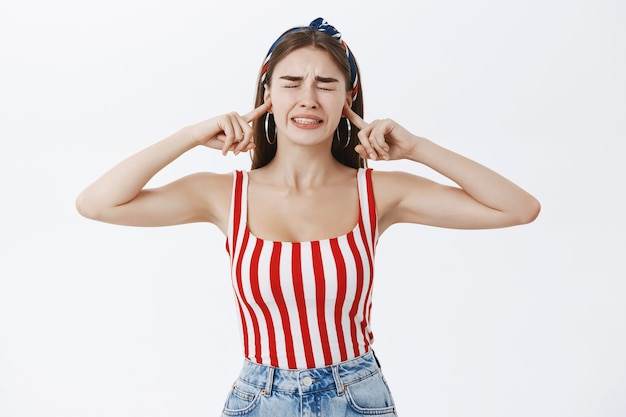 Free photo stylish woman irritated with pissing noise, being displeased closing eyes and clenching teeth from dislike closing ears with index fingers