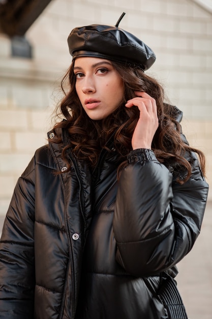 Free photo stylish woman posing in winter autumn fashion trend black puffer coat and leather hat beret in old beautiful street wearing high heel shoes