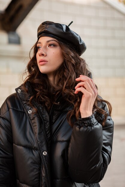 Stylish woman posing in winter autumn fashion trend black puffer coat and leather hat beret in old beautiful street wearing high heel shoes