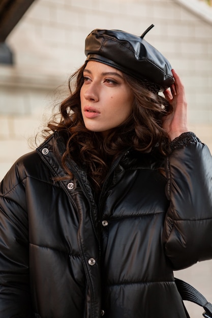 Free photo stylish woman posing in winter autumn fashion trend black puffer coat and leather hat beret in old beautiful street