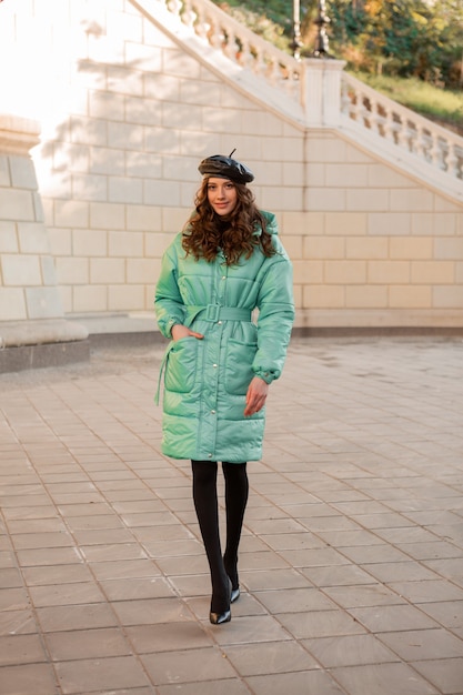 Free photo stylish woman posing in winter autumn fashion trend blue puffer coat and hat beret in old beautiful street full heigth