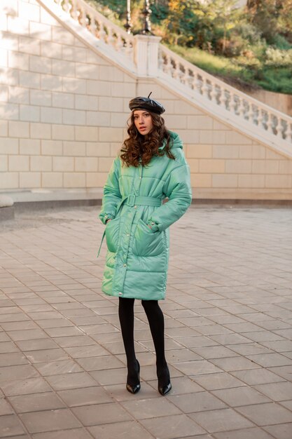 Stylish woman posing in winter autumn fashion trend blue puffer coat and hat beret in old beautiful street full heigth