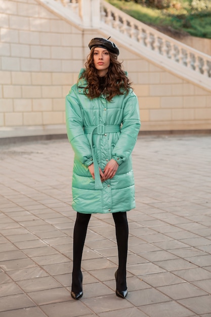 Free photo stylish woman posing in winter autumn fashion trend blue puffer coat and hat beret in old beautiful street full heigth