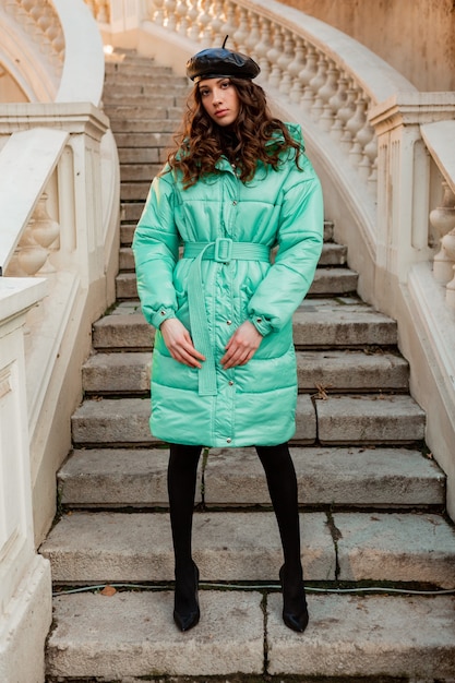 Free photo stylish woman posing in winter autumn fashion trend blue puffer coat and hat beret in old beautiful street stairs wearing high heel shoes