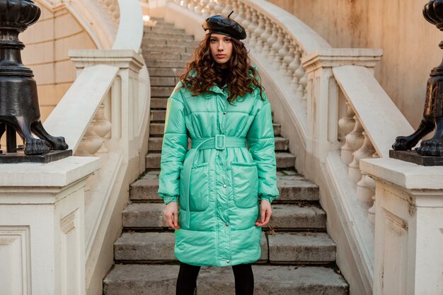 Stylish woman posing in winter autumn fashion trend blue puffer coat and hat beret in old beautiful street stairs