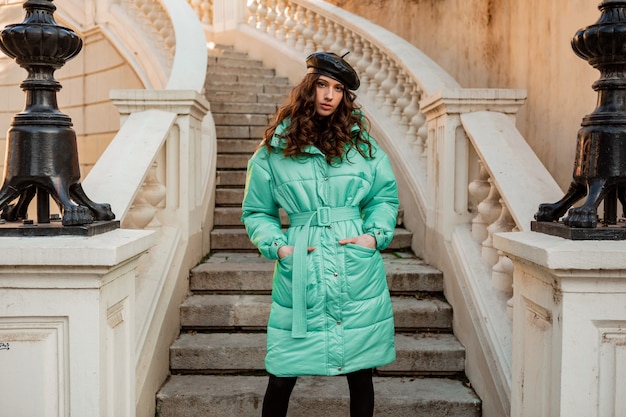 Stylish woman posing in winter autumn fashion trend blue puffer coat and hat beret in old beautiful street stairs