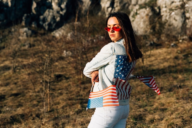 Stylish woman standing on nature with flags of United States