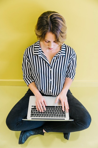 Free Photo stylish woman using laptop on yellow