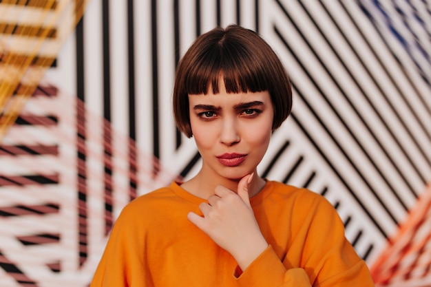 Free Photo stylish woman with brunette hair in bright sweatshirt posing on striped wall