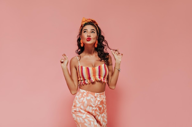 Free photo stylish woman with cool hairstyle in unusual bright earrings bandana and printed pants looking up on isolated background