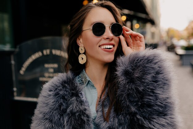 Stylish woman with dark hairs playfully posing on the street.