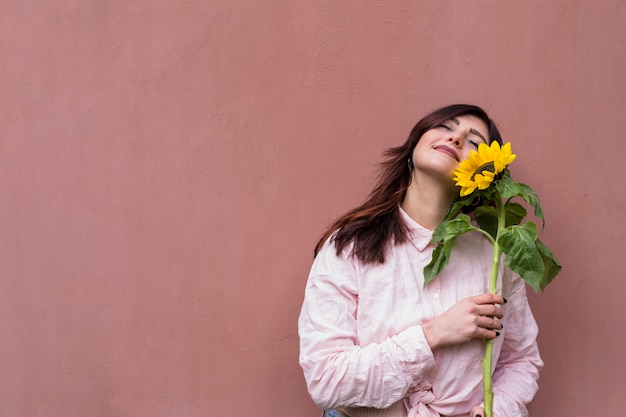 Stylish woman with sunflower in hands dreaming happily 