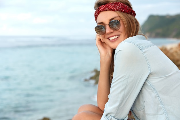 Free photo stylish woman with sunglasses sitting on the beach