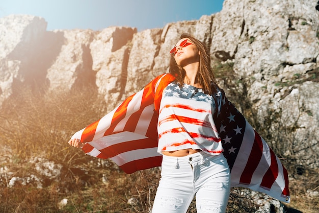 Free photo stylish woman wrapped in american flag in nature