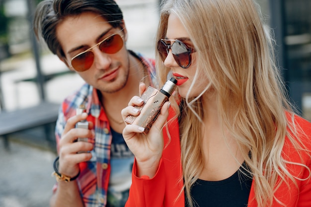 Stylish young couple with vape in a city