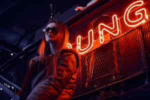 Free photo stylish young girl wearing a hoodie coat and sunglasses standing on stairs at underground nightclub with industrial interior