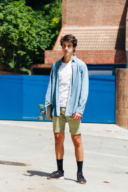 Free photo stylish young man holding skateboard standing outside