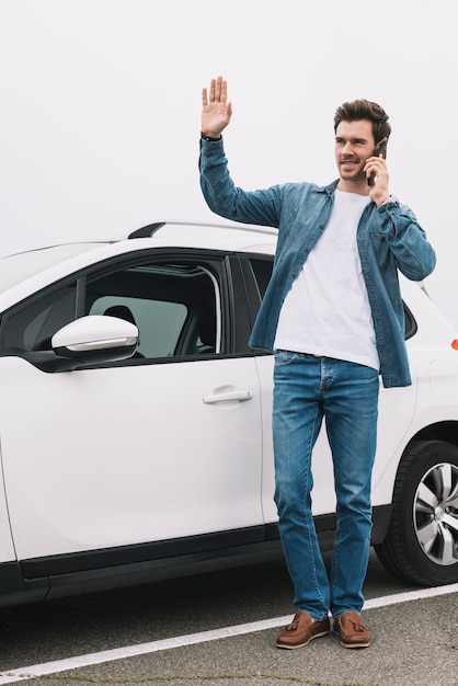 Stylish young man standing near the modern car waving his hand