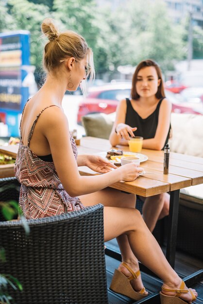 Stylish young woman drinking coffee with her friend