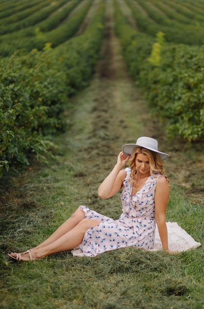 Stylish young woman in rose blue vintage dress and hat posing in green field