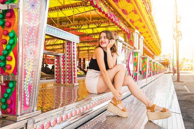 Stylish young woman sitting near the fairground ride