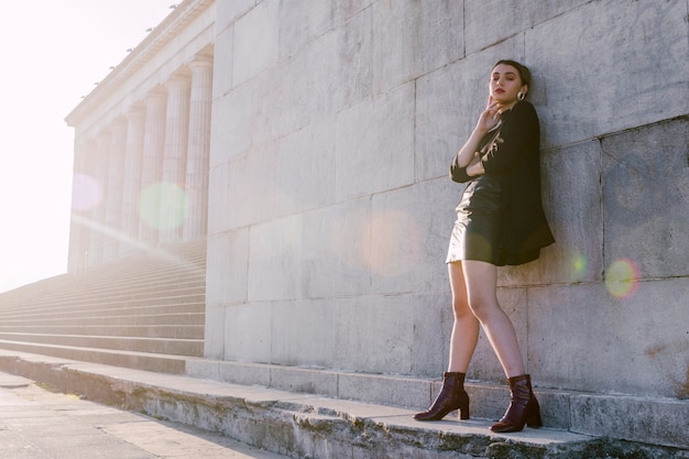 Free photo stylish young woman standing in wall with sunlight