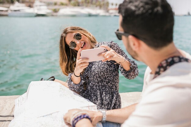 Stylish young woman taking picture of her boyfriend on jetty