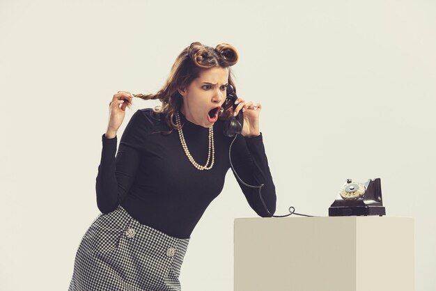 Free photo stylish young woman talkign on retro phone with expressive face isolated over white studio background retro style