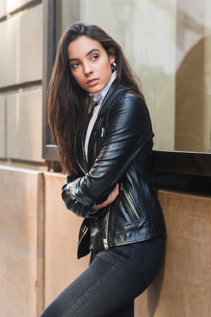 Stylish young woman with her crossed arms leaning on wall