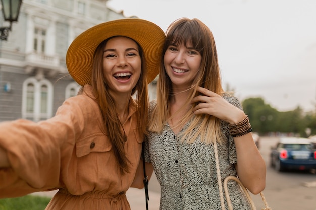 Free photo stylish young women traveling together in europe dressed in spring trendy dresses and accessories