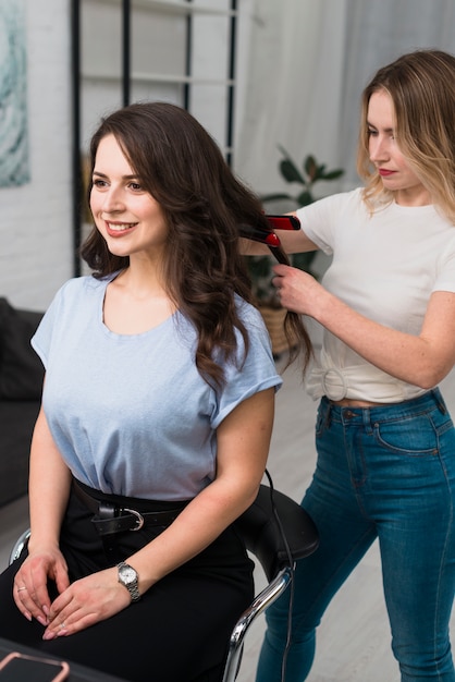 Stylist curling hair of young woman