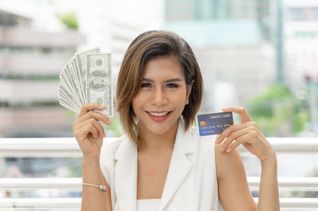 Successful beautiful Asian business woman holding money US dollar bills and credit card in hand 