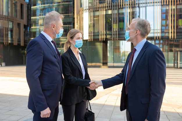 Free Photo successful business people standing near office buildings, shaking hands, meeting and talking in city. closeup, low angle. communication and partnership concept