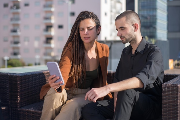 Free photo successful business people on terrace roof. man and woman in formal clothes sitting on terrace roof, looking at mobile phone, sitting on rattan sofa. work, modern technology, team concept