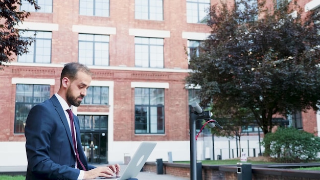 Free photo successful businessman in suit working at marketing presentation sitting on bech outside in front of corporate building office. executive manager searching information on internet.