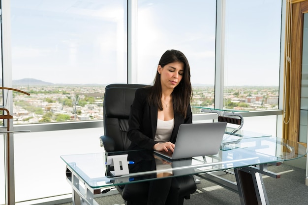 Successful and busy female boss working hard to achieve her business goals while typing on her laptop at a modern office desk