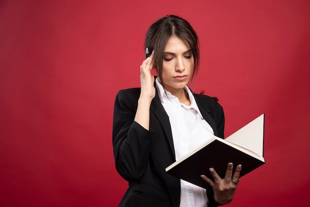 Successful employee reading her memory book on red background. 