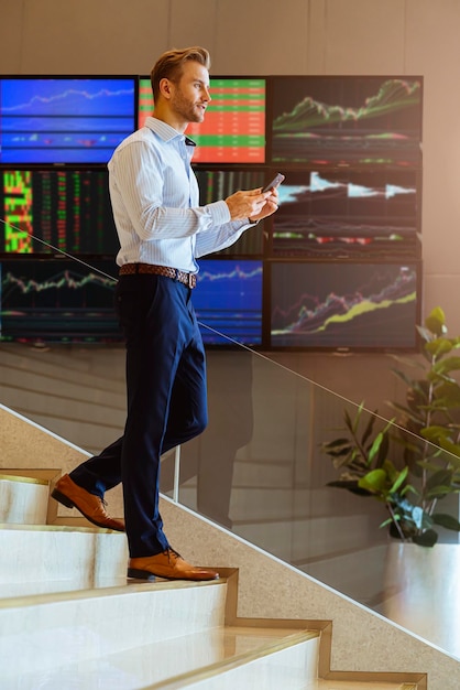 Free Photo successful smart caucasian businessman walking on stair trade stock with smartphone communicate with happiness and enthusiastic modern office background