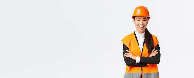 Successful smiling asian female engineer architect in safety helmet jacket cross arms chest and laug