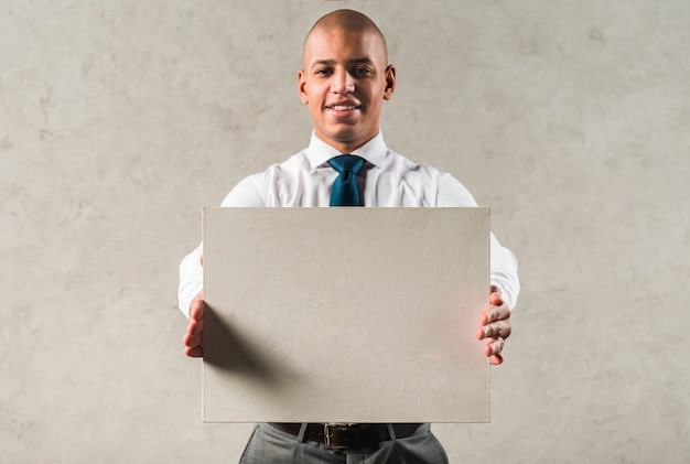 Free Photo successful young businessman showing grey placard standing against wall