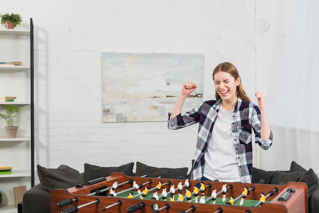 Successful young woman standing near the table soccer game clenching her fist