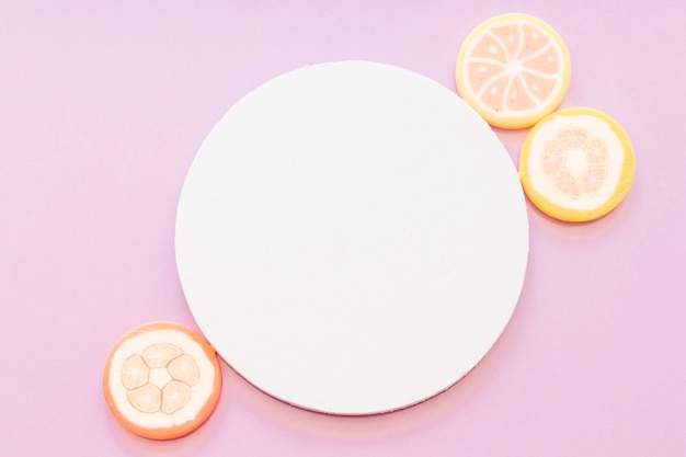 Free photo sugar jelly candies near the white blank circular frame on pink backdrop