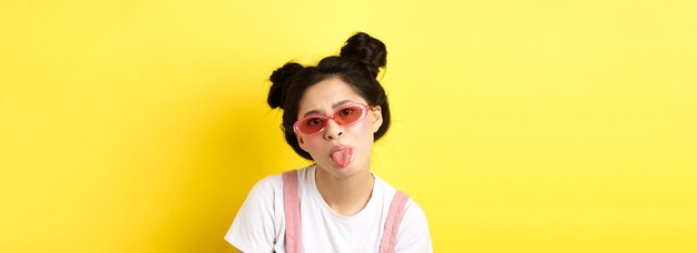 Summer and beauty concept childish asian girl in sunglasses showing tongue being rude standing on ye