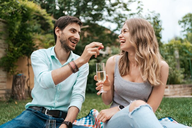 Summer holidays, people, romance, man and woman feeding each other strawberries while drinking sparkling and enjoying time together at home