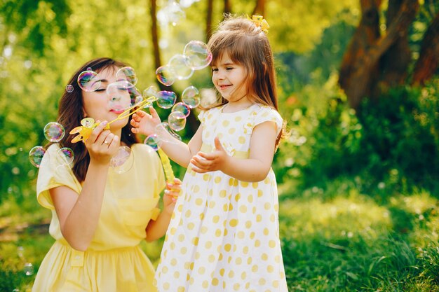 in a summer park near green trees, mom walks in a yellow dress and her little pretty girl