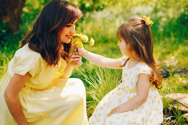 in a summer park near green trees, mom walks in a yellow dress and her little pretty girl