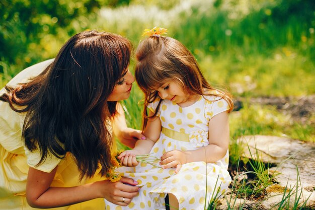 in a summer park near green trees, mom walks in a yellow dress and her little pretty girl