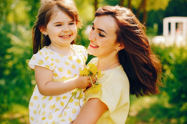 in a summer park near green trees, mom walks in a yellow dress and her little pretty girl