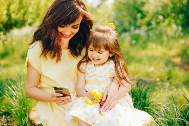 in a summer park near green trees, mom walks in a yellow dress and her little pretty girl