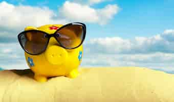 Free photo summer piggy bank with sunglasses on the beach